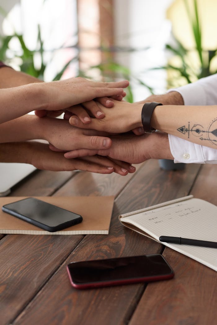 about-img Hands from a diverse team stack on a table symbolizing unity and teamwork in a modern office setting.